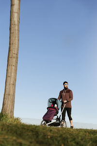 Man walking with baby stroller on field against sky