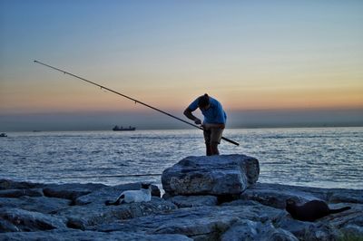 Rear view of man fishing at sea shore against sky