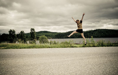 Full length of woman jumping on road against sky