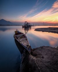 Boats moored at beach against sky during sunset