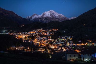 Illuminated town by mountains against sky at night