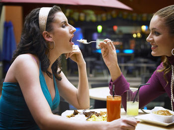 Woman feeding female friend while sitting at outdoor cafe