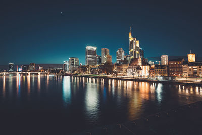 Illuminated buildings by river against sky at night