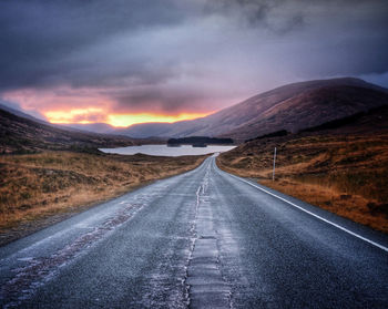 Country road leading towards mountains against sky