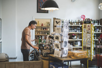 Side view of male sales clerk standing at checkout counter in deli