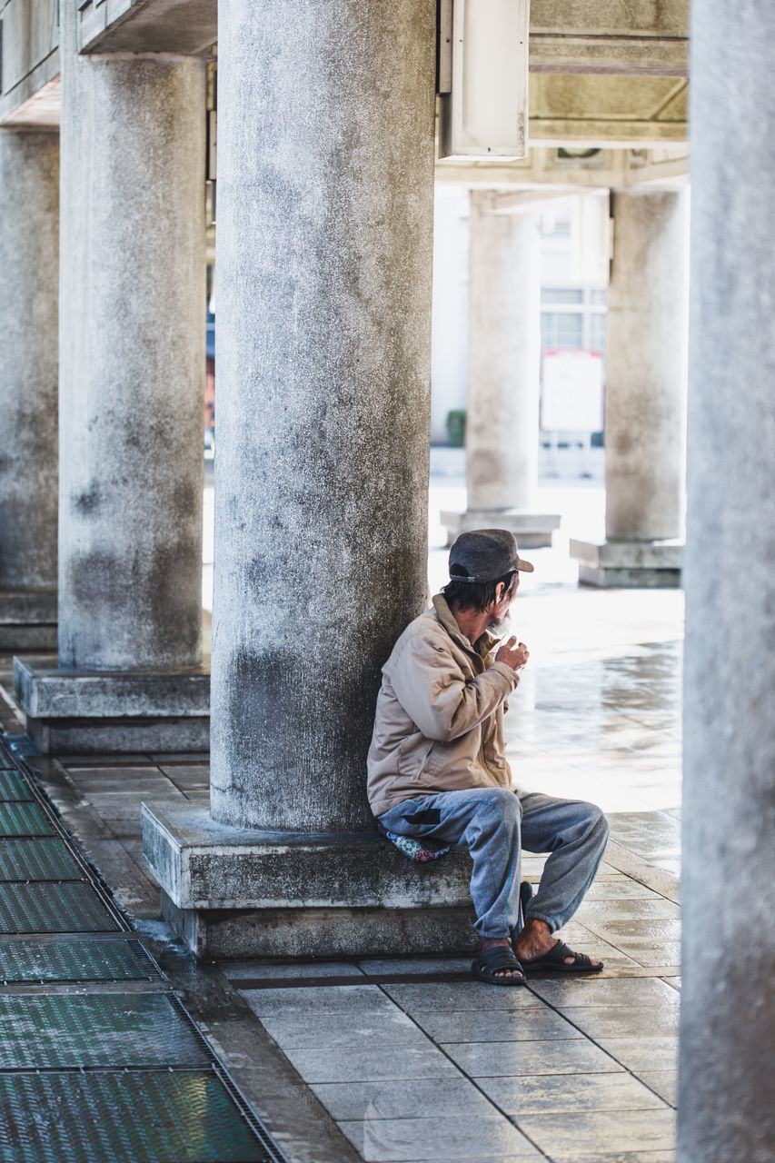 SIDE VIEW OF YOUNG MAN SITTING ON COLUMN
