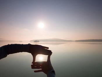 Man hand makes shadow symbols to sun. misty daybreak at a beautiful peaceful lake.