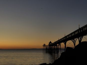 Silhouette bridge over sea against clear sky during sunset