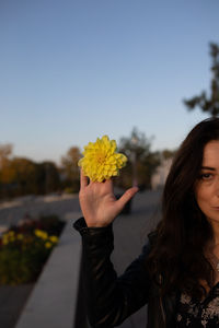 Portrait of beautiful woman holding yellow flower against sky