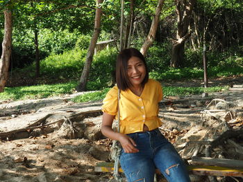 Portrait of smiling young woman sitting on land in forest