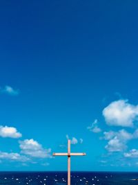 Low angle view of cross by sea against blue sky