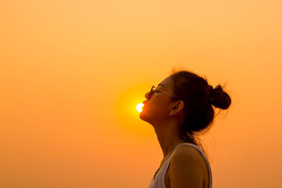 Optical illusion of young woman kissing sun against clear orange sky