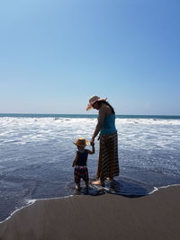 Mother and son standing on shore against blue sky