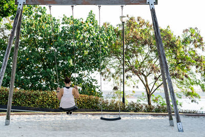 Rear view of woman sitting by plants against trees