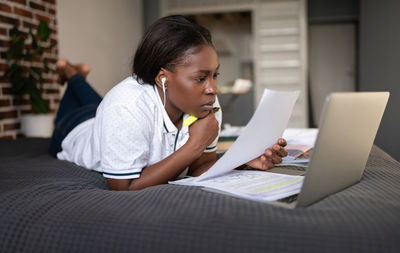 Thoughtful black woman reading paper during online lesson