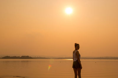 Woman standing in sea against sky during sunset