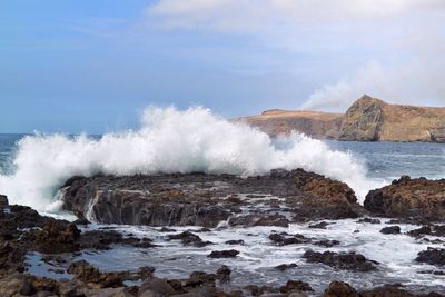 Waves splashing on rocks against sky