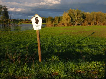 Information sign on field by trees against sky