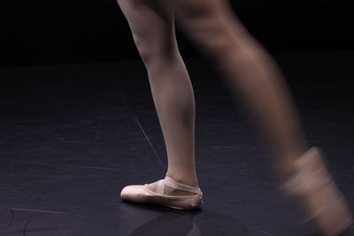 Low section of ballet dancer dancing against black background
