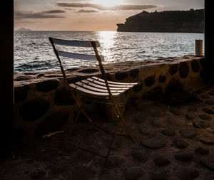 Chairs on beach against sky during sunset