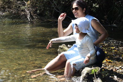 Adult woman with a child sitting on rock by lake in forest throughing rock in the water