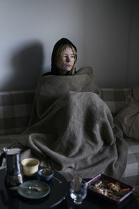 Teenage girl sitting on sofa wrapped in blanket