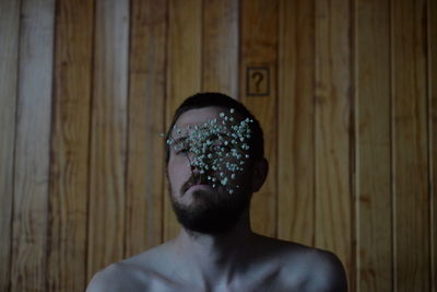 Portrait of shirtless man in wooden wall, with flowers