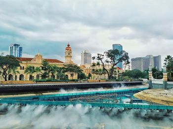 Buildings by swimming pool in city against cloudy sky