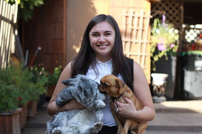 Portrait of smiling woman with dog and rabbit standing on footpath