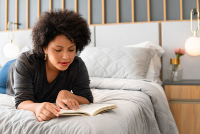 Young woman using phone while sitting on bed at home