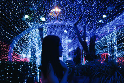 Side view of woman standing against illuminated lighting