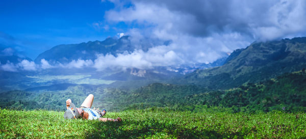 Rear view of woman sitting on mountain against sky
