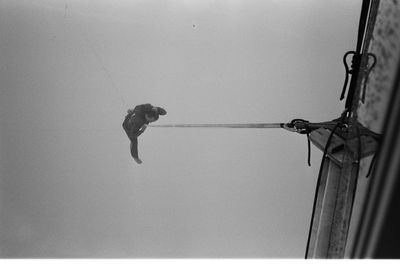 Low angle view of man hanging on rope against wall