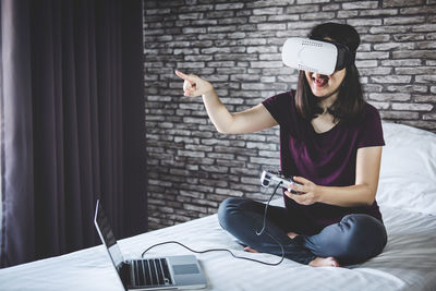 Woman wearing virtual reality simulator while sitting on bed at home