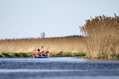 People kayaking in lake against clear sky