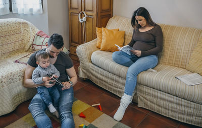 Full length of siblings sitting on sofa at home