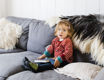 Portrait of girl holding book while sitting on sofa at home