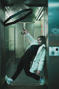 Young woman holding umbrella standing against wall