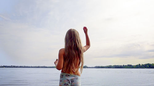 Shirtless girl standing at lakeshore against sky