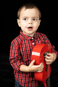 Portrait of cute boy holding camera over black background