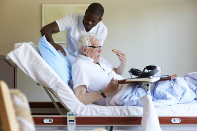 Male nurse adjusting pillow for senior man on bed in hospital ward