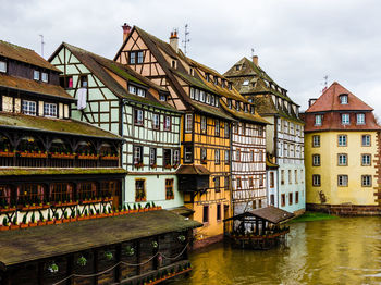 Half-timbered houses by canal in city against sky