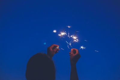 Rear view of woman holding sparklers against clear sky at night