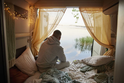 Man sitting in camper van and looking at lake