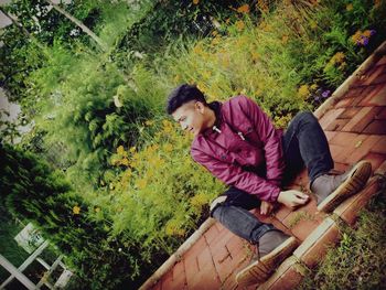 Full length of young man looking away while sitting on footpath