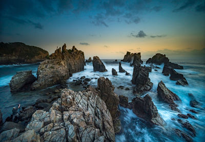 Rocks in sea against sky during sunset