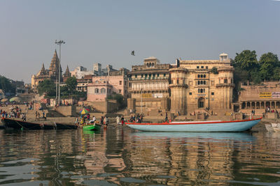 Boats moored in river by buildings against clear sky