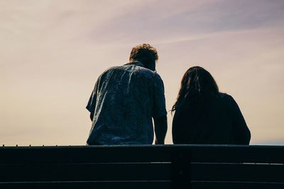 Low angle view of man and woman sitting against sky on sunny day