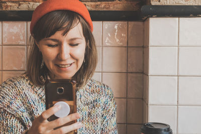 Smiling young woman using mobile phone against wall