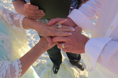 Low section of priest with bride and bridegroom holding hands while standing at beach during wedding ceremony